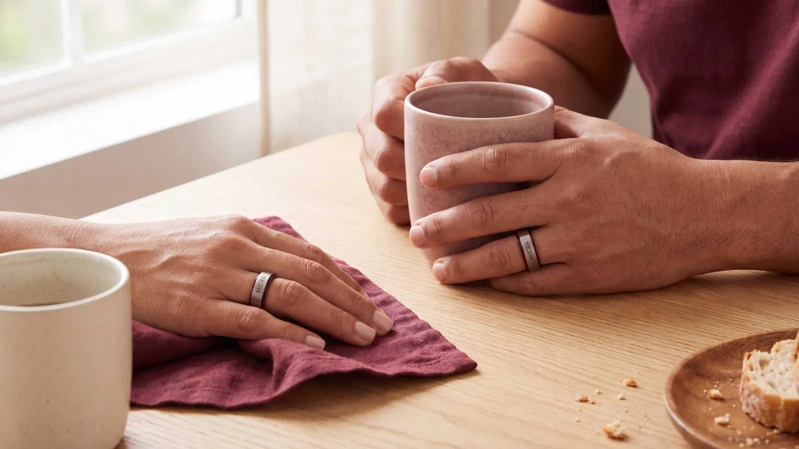 Manos de dos personas con anillos inteligentes MICRA sobre una mesa de madera, luz de mañana